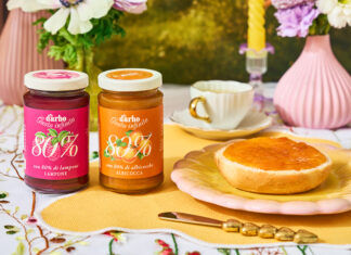 Due vasetti di confettura Darbo 80% frutta ai gusti lampone e albicocca su una tavola imbandita per la colazione con pane tostato, fiori freschi e un'atmosfera naturale e solare