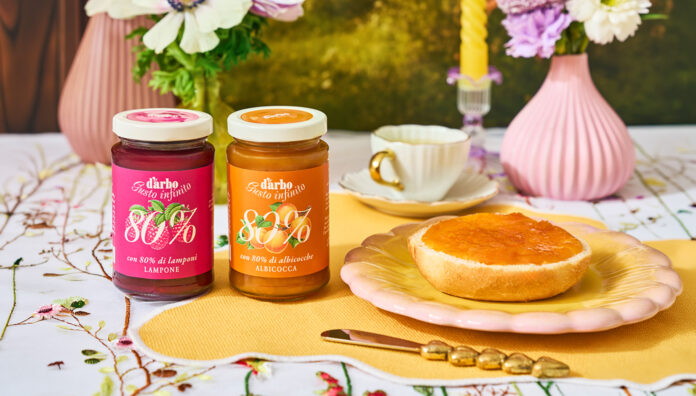 Due vasetti di confettura Darbo 80% frutta ai gusti lampone e albicocca su una tavola imbandita per la colazione con pane tostato, fiori freschi e un'atmosfera naturale e solare