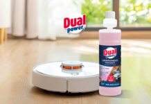 Dual Power accelera sulla detergenza tech Flacone di detergente Dual Power Lavapavimenti Profumato specifico per robot domestici, posizionato su un pavimento in legno accanto a un robot lavapavimenti bianco in funzione