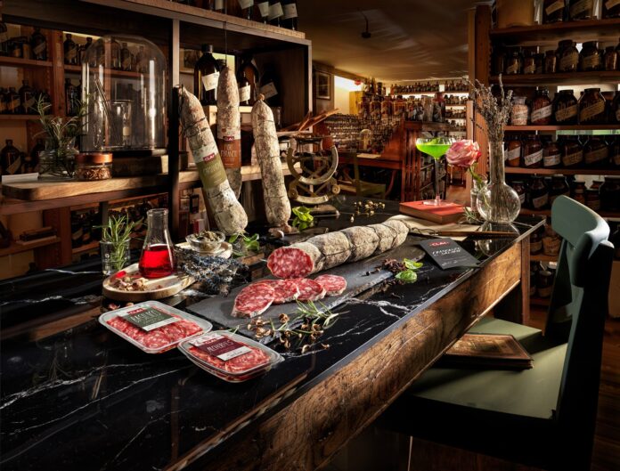 Clai Fragranze Cardamomo FioriArancio Salami Vaschette 2026 Presentazione della linea Fragranze di Salame CLAI sul bancone di un laboratorio olfattivo, con salami interi al Cardamomo e Fiori d'Arancio e le nuove vaschette affettati al Basilico e Alchermes
