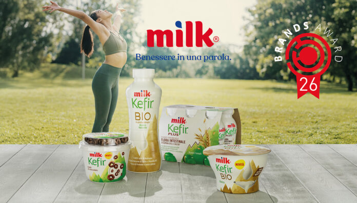 Milk Kefir 2026 Prodotti della gamma Milk Kefir da bere e al cucchiaio di Latteria Nöm in un parco con il bollino del premio Brands Award 2026 e una donna che fa stretching