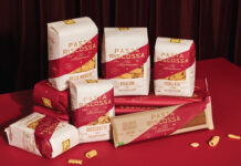 Pasta Riscossa, la rivincita della qualità Confezioni assortite di Pasta Riscossa Collezione Premium, tra cui Mezze Maniche, Rigatoni, Orecchiette e Pasta Integrale, in esposizione su un piano rosso con sfondo drapery scuro, con etichette chiare che specificano "grano 100% italiano"