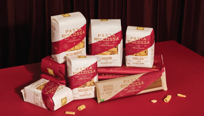 Pasta Riscossa Collezione Premium 2026 Confezioni assortite di Pasta Riscossa Collezione Premium, tra cui Mezze Maniche, Rigatoni, Orecchiette e Pasta Integrale, in esposizione su un piano rosso con sfondo drapery scuro, con etichette chiare che specificano