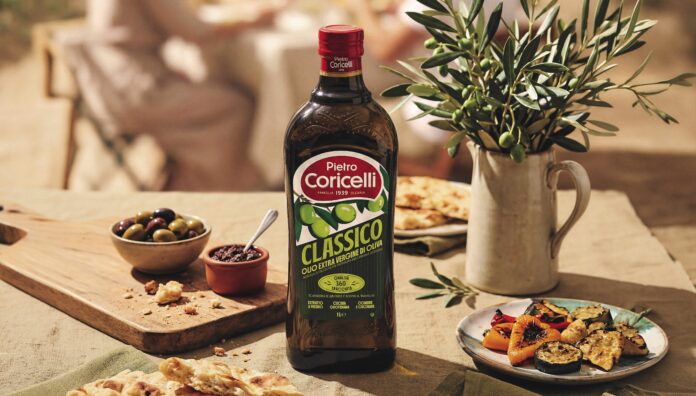 Bottiglia di Olio Extra Vergine di Oliva Classico Pietro Coricelli con la nuova grafica e packaging frutto del rebranding aziendale, posizionata su una tavola estiva con pietanze e rami di olivo
