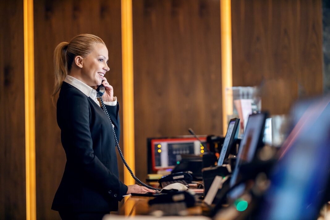receptionist sorridente al telefono mentre utilizza un software gestionale per hotel alla reception di una struttura moderna e di design
