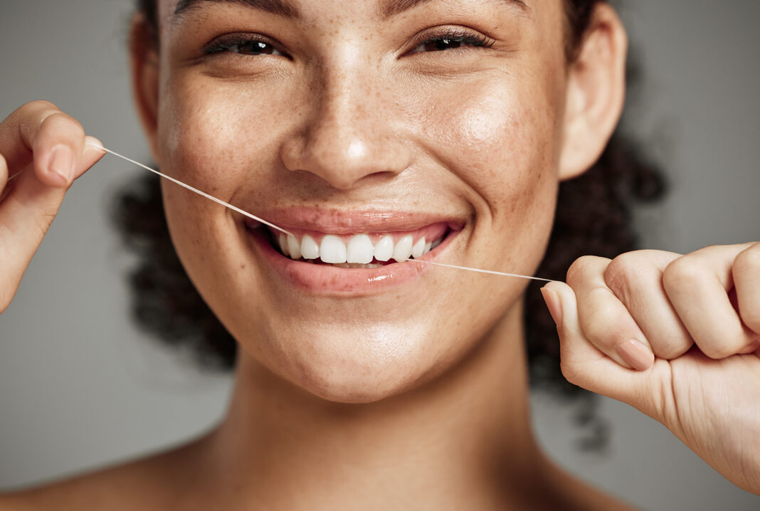 Woman portrait, dental floss and flossing teeth with smile for oral hygiene, health and wellness on studio background. Face of female happy about self care, healthcare and grooming for healthy mouth Controllo del biofilm