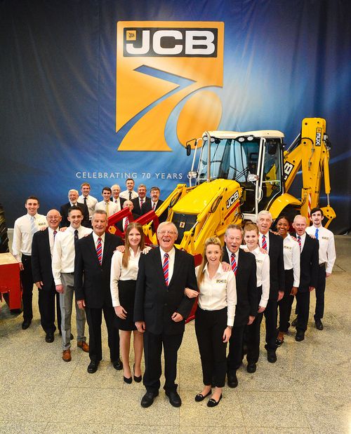 Giovani laureati apprendisti in JCB (con le camicie bianche) e dipendenti in pensione che ora lavorano in JCB come guide turistiche della fabbrica (con le giacche blu)
