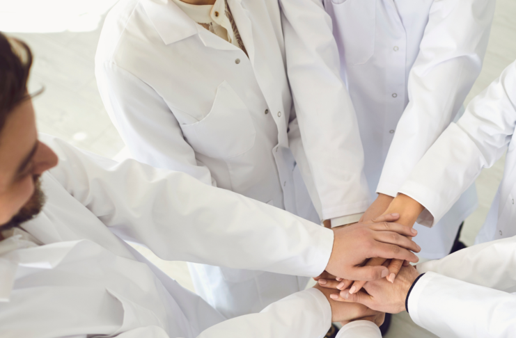 Giornata del personale sanitario: il valore del team multidisciplinare nella gestione della complessità Professionisti sanitari in camice bianco con le mani unite in segno di collaborazione