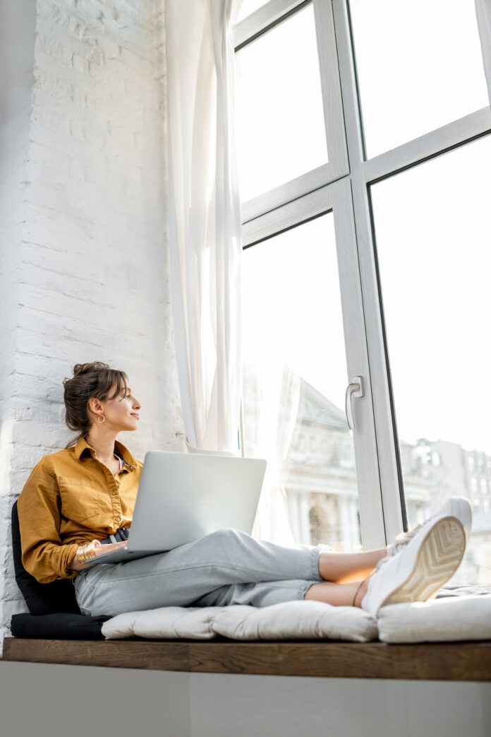 Young,Woman,Dressed,Casually,Working,On,Laptop,While,Sitting,On