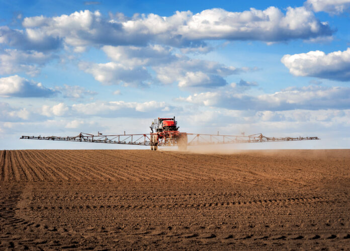 barra_Big red sprayer with long arms at the arable field makes fertilizers in early spring view with clouds difesa